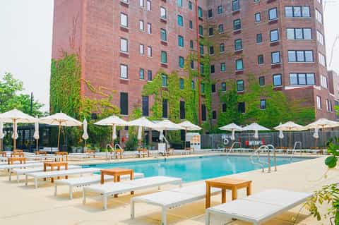 Urban pool deck with lounge chairs, umbrellas, ivy-covered brick building, and bright turquoise water