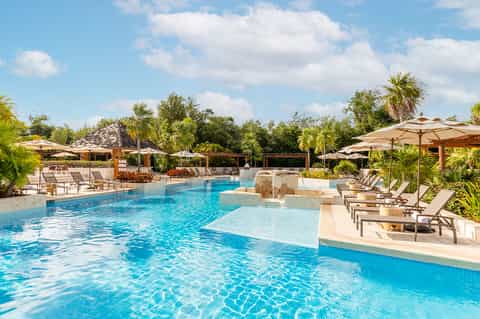 Resort pool with loungers, umbrellas, shallow lounge area, and tropical landscape