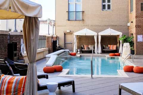 Urban hotel rooftop pool with white cabanas, orange accents, and brick building architecture