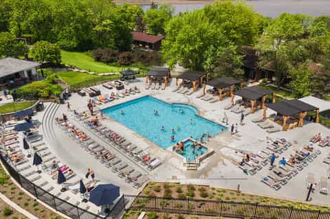 Aerial view of resort pool complex surrounded by lounge chairs, umbrellas, and forested grounds