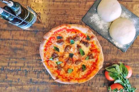 Freshly baked pizza with toppings on wooden table, accompanied by beverages and mozzarella