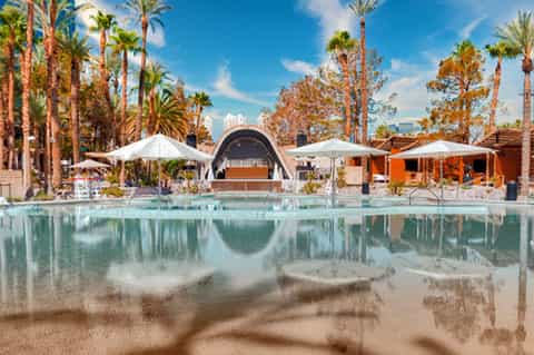 Contemporary resort pool with palm trees, white umbrellas, orange building, and urban skyline