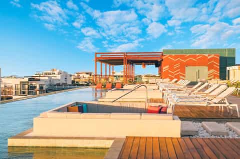 Modern rooftop pool deck with orange structural elements, lounge seating, and waterfront views