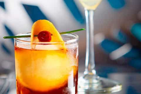 Tropical cocktail with orange slice and cherry garnish on ocean backdrop