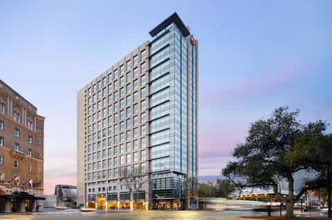 Modern hotel high-rise building with tan and glass facade at dusk with street-level retail