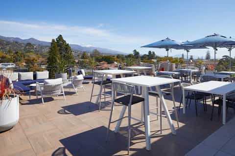 Expansive rooftop terrace with high-top tables, lounge seating, umbrellas, and mountain views