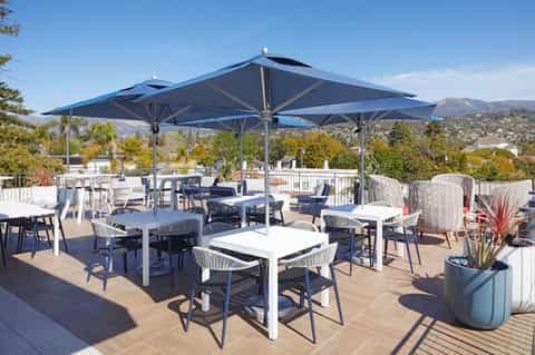 Rooftop terrace with large umbrellas, white tables, and mountain views with landscaping