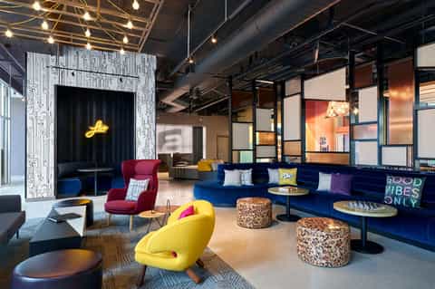 Modern hotel lobby lounge with colorful seating, neon signage, pendant lighting, and contemporary furniture