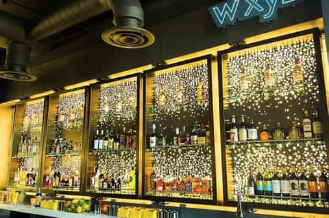 Illuminated bar shelves displaying bottles with decorative pearl-dotted backlit wall panels