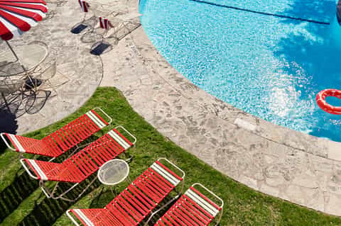 Red and white striped lounge chairs on green grass next to sparkling blue swimming pool