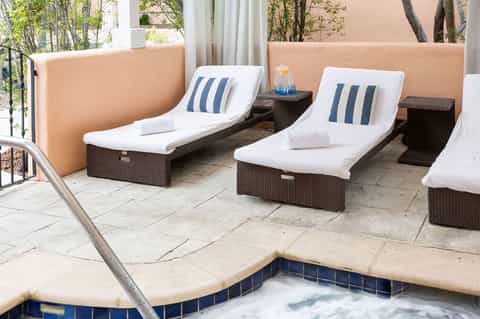 Two lounge chairs with striped pillows overlooking small jacuzzi tub on terrace patio