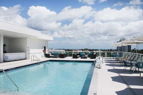 Rooftop pool deck with ocean views, lounge chairs, and white umbrellas