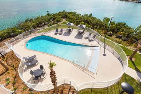 Curved pool overlooking turquoise ocean water with lounge chairs and palm trees