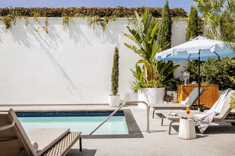 Modern resort pool with lounge chairs, white umbrella, and tropical landscaping
