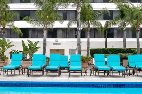 Hotel poolside with turquoise lounge chairs, palm trees, and white building facade
