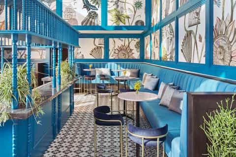 Turquoise-framed conservatory lounge with botanical wallpaper and blue upholstered seating