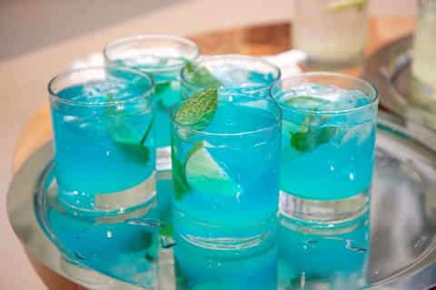 Four bright turquoise cocktails with mint leaves on a round tray