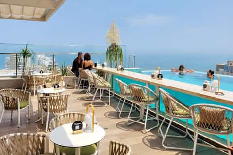 Upscale rooftop pool bar overlooking turquoise water and ocean coastline with woven chairs