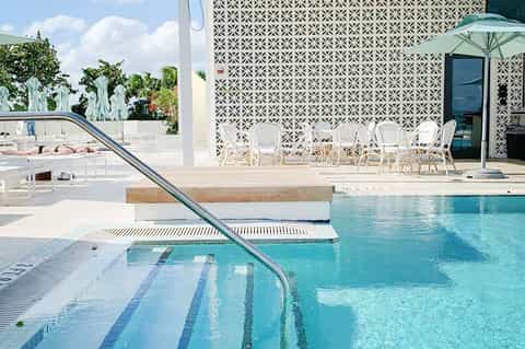 Modern resort pool area with lane markings, geometric patterned wall, white lounge chairs, and umbrella