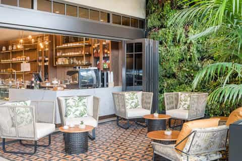 Elegant outdoor cafe with woven chairs, wood tables, lush green living wall, and indoor bar