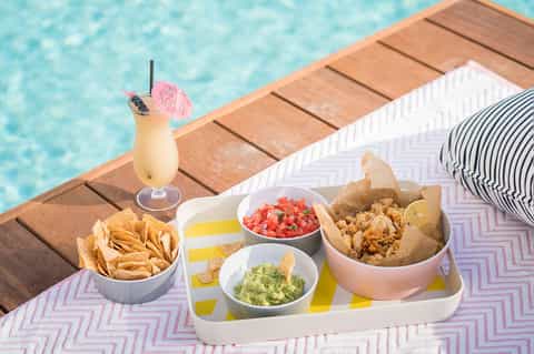 Poolside snack platter with chips, dips, and cocktail with pink umbrella garnish