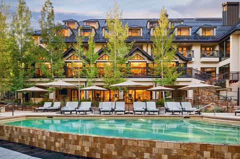 Modern mountain resort with lit windows, pool area with loungers, and autumn foliage
