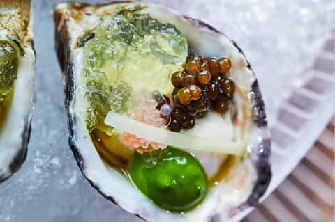 Freshly shucked oyster topped with caviar and cucumber garnish on ice