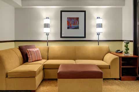 Hotel suite living area with yellow sectional sofa, ottoman, and decorative wall art