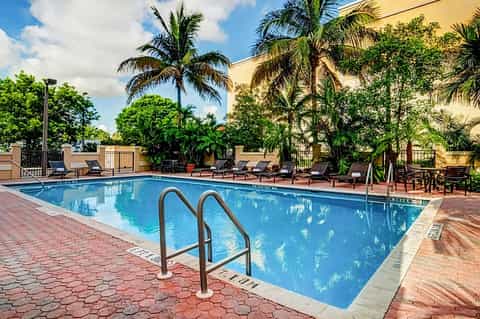 Resort swimming pool with ladder, lounge chairs, palm trees, and tropical courtyard setting