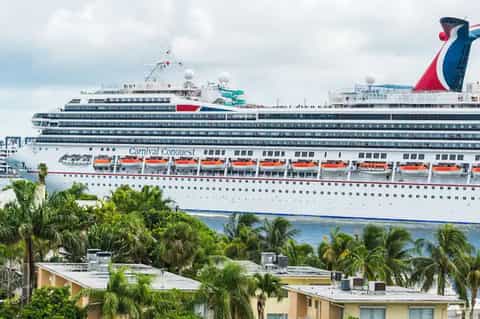Large cruise ship Carnival Conquest docked at tropical port with palm trees and buildings