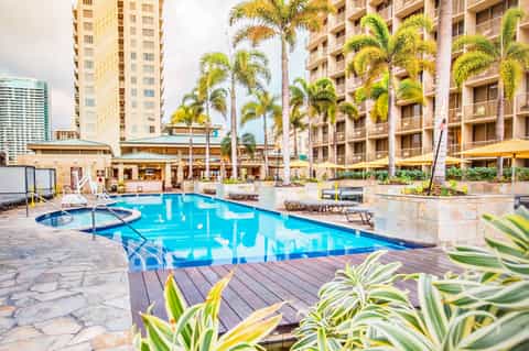 Resort courtyard with crystal blue swimming pool, palm trees, and multi-story tan residential buildings