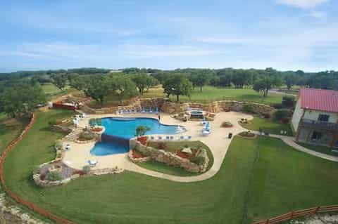 Aerial view of luxury resort with resort pool, lazy river, manicured lawns, oak trees, and country setting