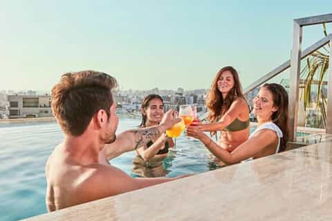 Group toasting with orange cocktails in infinity pool overlooking city skyline