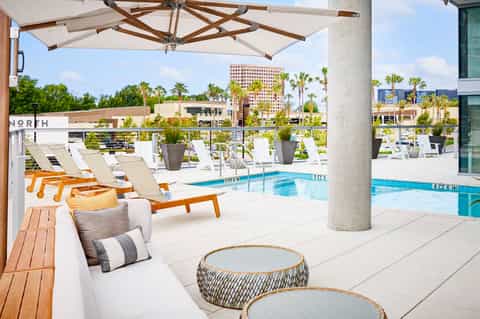 Modern rooftop pool deck with orange loungers, umbrellas, and city skyline views