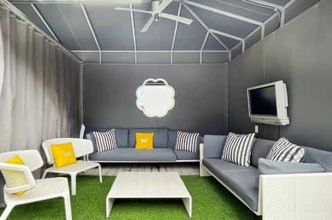 Contemporary indoor lounge space with gray sofas, striped pillows, retractable roof, and green floor