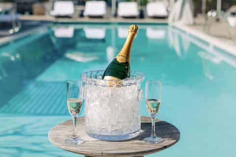 Champagne bottle chilling in ice bucket with two glasses at poolside table
