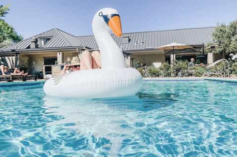 Guest on giant swan pool float in resort pool near house
