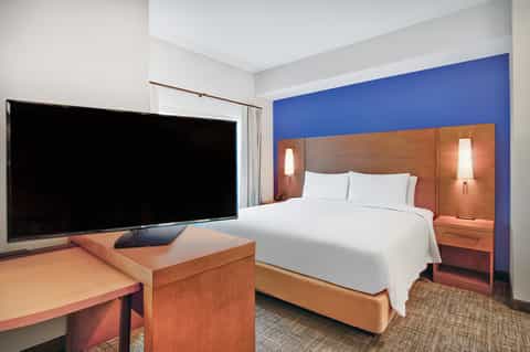 Modern hotel bedroom with orange wood headboard, blue accent wall, and large TV