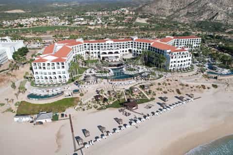 Aerial view of large beachfront resort complex with red roofs and mountain backdrop