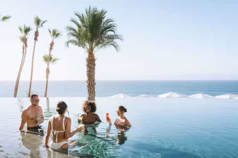 Guests swimming in infinity pool with palm trees and ocean horizon backdrop