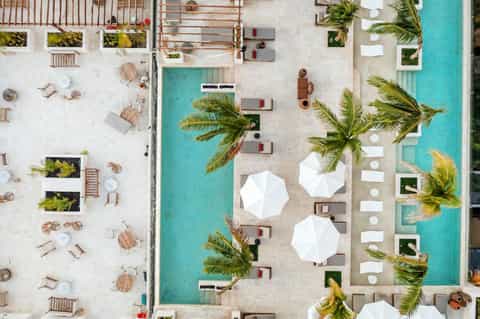 Overhead view of resort pool surrounded by white umbrellas, palm trees, and lounge chairs