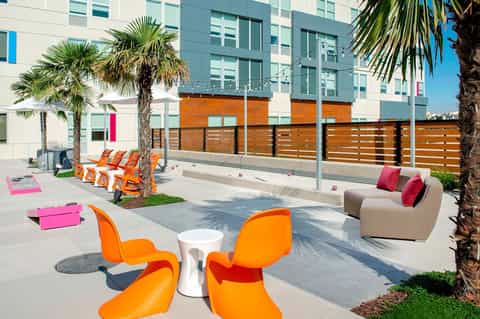 Colorful modern courtyard with orange loungers, palm trees, and apartment building