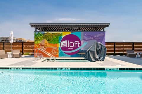 Modern hotel pool with colorful branded wall, pergola shade structure, and wood fence