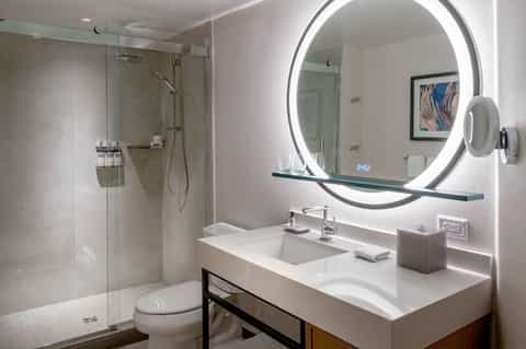 Modern bathroom with circular illuminated mirror, glass shower, and white vanity