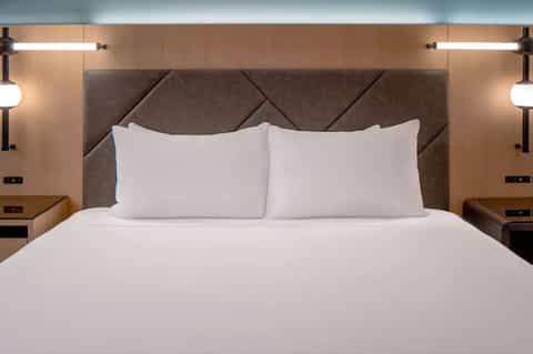 Clean hotel bed with white linens, geometric headboard, and bedside lighting