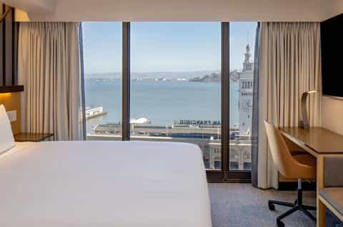 Luxury hotel bedroom with panoramic bay and ferry terminal views through floor-to-ceiling windows