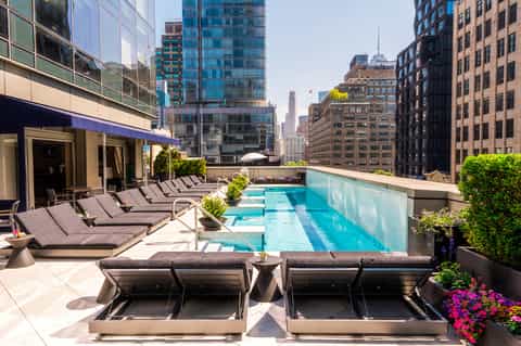 Rooftop pool with city skyline views, lounge chairs, and modern urban high-rise buildings