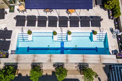Overhead view of rectangular lap pool with black loungers and blue umbrellas on concrete deck