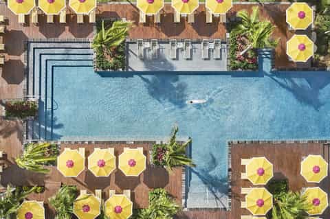 Aerial view of resort pool deck with bright yellow umbrellas, palm landscaping, and wood decking