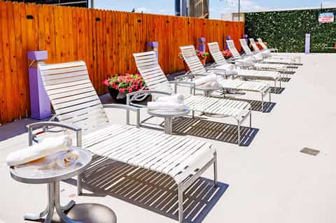 Row of white lounge chairs along an orange wood fence at a hotel pool deck with flowers